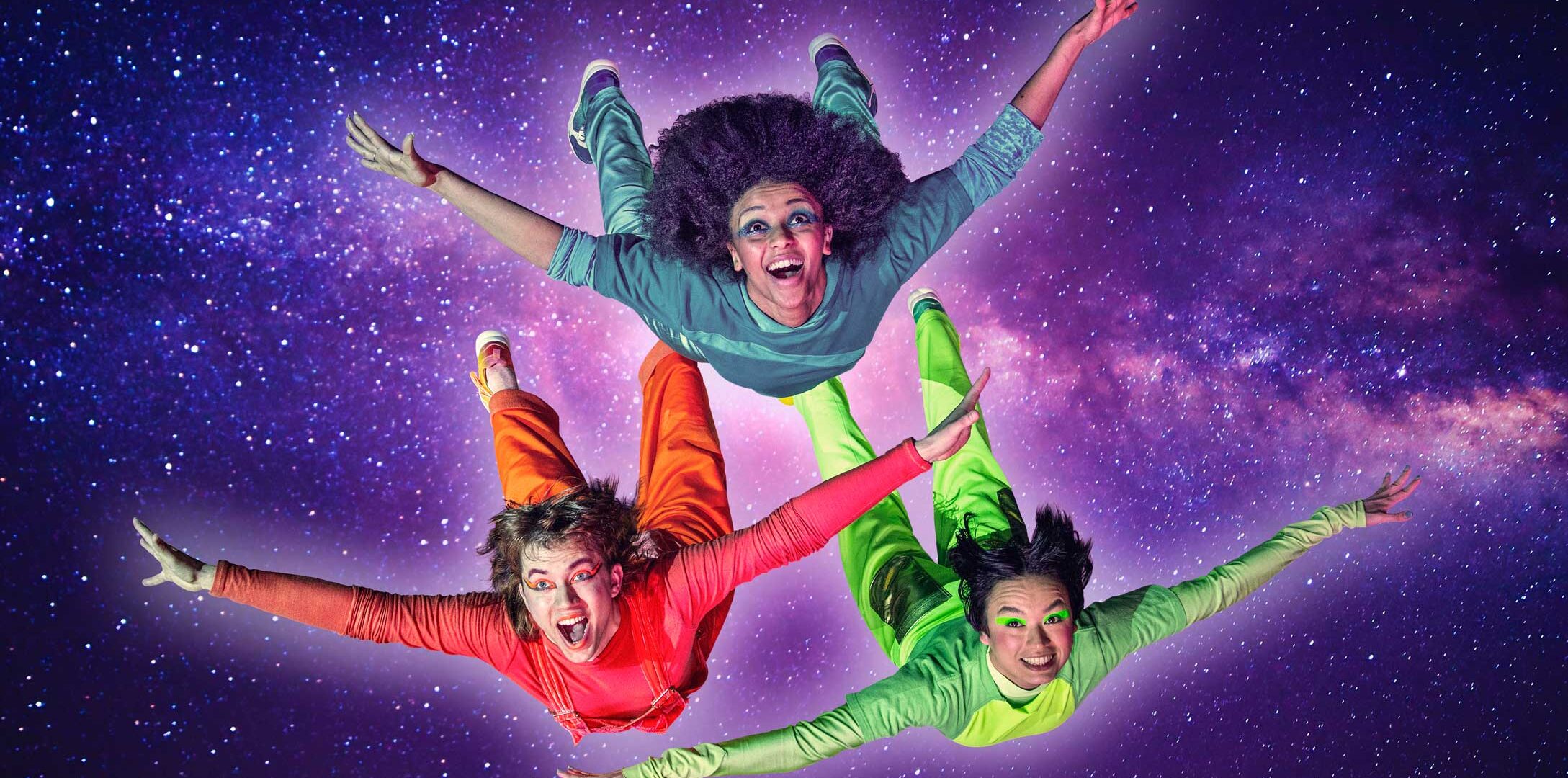 Kolme tanssijaa värikkäissä vaatteissa lentää kohti kameraa, taustalla avaruus.