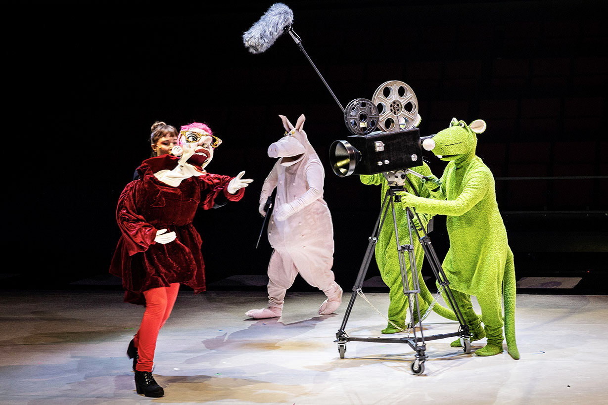 Nukettaja, isokokoinen nukkehahmo, sikahahmo ja kaksi rottahahmoa esittävät elokuvan kuvaamista ison videokameran kanssa.